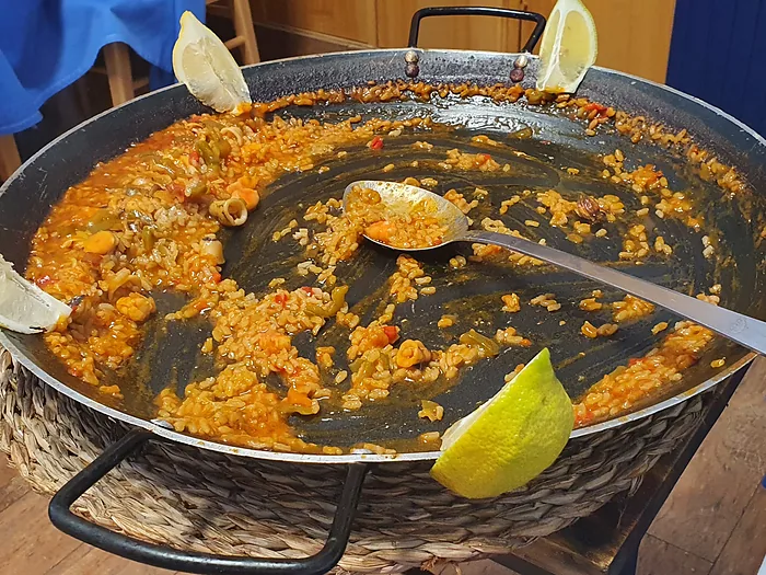 Paellera con paella recién hecha y dos gajos de limón al borde.