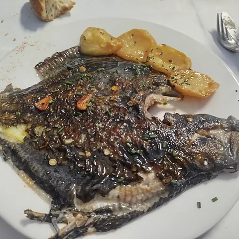 Pescado abierto y hecho a la parrilla, con refrito y patata por encima.
