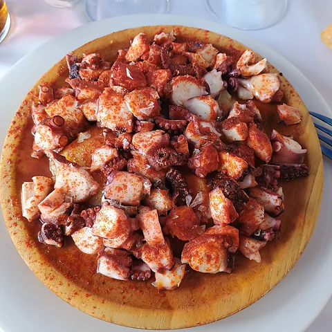 Pulpo a la gallega servido sobre una tabla redonda de madera.