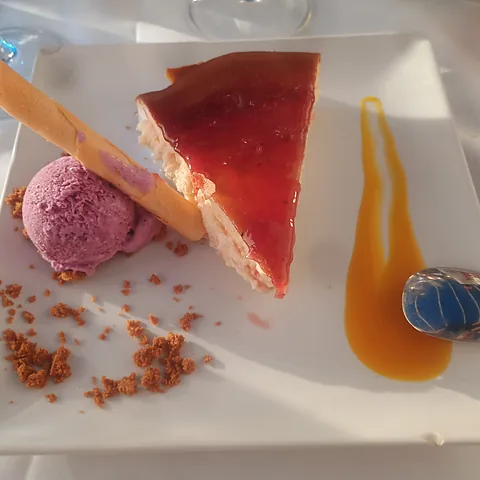 Porción de tarta de queso con mermelada, una bola de helado y una teja de galleta.